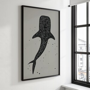 Minimalist illustration print depicting a whale shark swimming in the ocean in an elegant manner, the shark is drawn in a black color with white dots and the background is a beige color with black ink spots, it is hanging in a living room