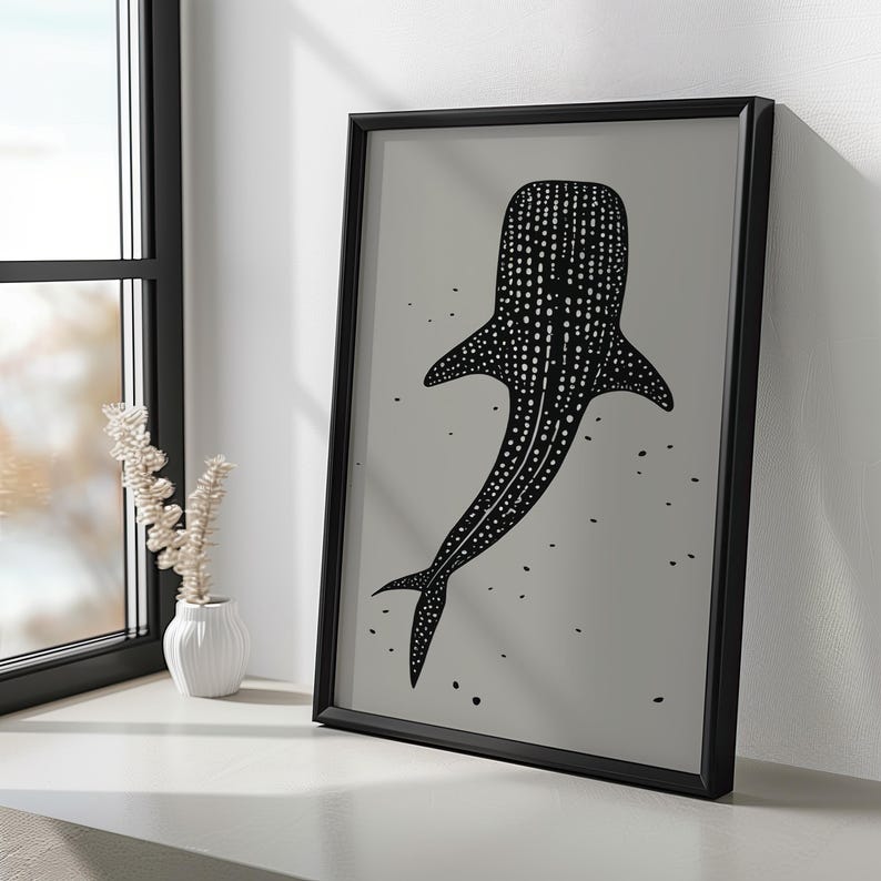 Minimalist illustration print depicting a whale shark swimming in the ocean in an elegant manner, the shark is drawn in a black color with white dots and the background is a beige color with black ink spots, it is hanging in a modern living room