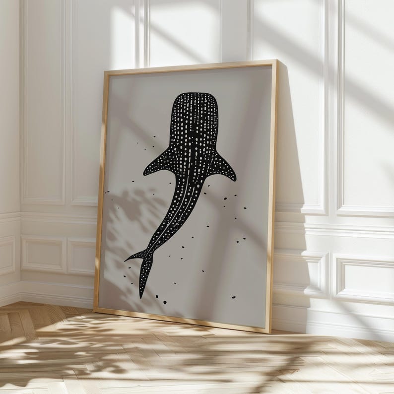 Minimalist illustration print depicting a whale shark swimming in the ocean in an elegant manner, the shark is drawn in a black color with white dots and the background is a beige color with black ink spots, it is hanging in a dining room