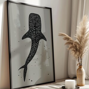 Minimalist illustration print depicting a whale shark swimming in the ocean in an elegant manner, the shark is drawn in a black color with white dots and the background is a beige color with black ink spots, it is hanging in a modern kitchen