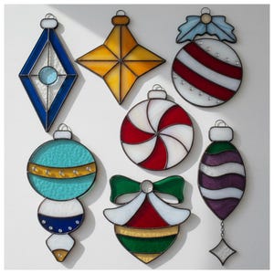 May include: A collection of colorful stained glass Christmas ornaments in various shapes. The ornaments include a blue diamond, a yellow star, a red and white striped ball, a red and white swirl, a teal and gold ornament, a green and white bow, and a purple teardrop.