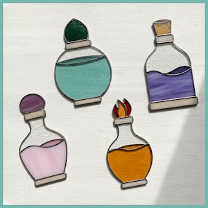 May include: Four stained glass potion bottle ornaments in various colors: teal, purple, pink, and orange. Each bottle has a unique stopper or flame design. The bottles are outlined in silver and set against a white background.