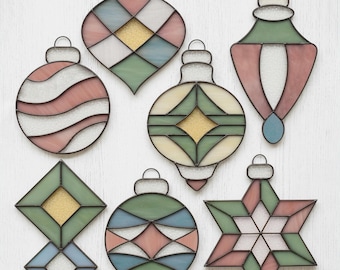 Könnte beinhalten: Eine Sammlung von sieben Weihnachtsornamenten aus Buntglas in verschiedenen Formen. Die Ornamente weisen Pastellfarben wie Rosa, Grün und Blau mit goldenen Glitzerakzenten auf. Jedes Ornament hat eine Metallschlaufe zum Aufhängen.