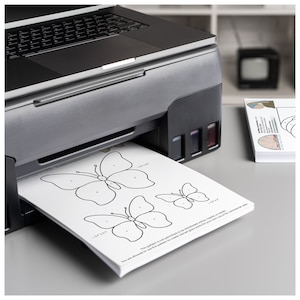 May include: A black and silver printer with a sheet of paper coming out of the paper tray. The paper has a black and white butterfly design with numbers on it. The text on the paper reads "This pattern is not permitted to be distributed online, copied or resold. You are allowed to use this pattern to create canvas, glass, wood, or other crafts for your own use or for commercial sale."