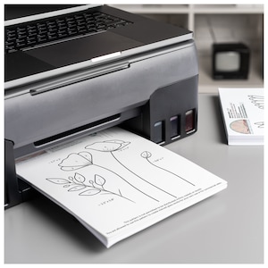 May include: A black and silver inkjet printer with a white sheet of paper with a flower design and numbers printed on it. The paper is being fed into the printer. The text on the paper reads "This pattern is not permitted to be distributed, copied or resold. You are allowed to use this pattern to create finished works for your own use or for commercial sale."