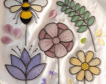 May include: A collection of five stained glass garden stakes featuring a yellow and black bee, a green leaf sprig, a pink flower, a purple lotus-style flower, and a yellow daisy with a white dotted center, all with dark metal soldering.