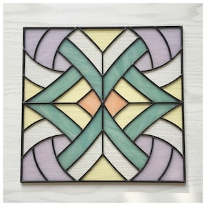 May include: Square stained glass panel with a geometric design. The panel features a symmetrical pattern of pastel colors, including lavender, yellow, and mint green, framed by black lines. The center has a peach-colored diamond shape.