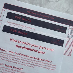 Peut inclure: Une feuille de papier blanche avec le titre "Comment rédiger votre plan de développement personnel" et une liste d'étapes à suivre. Le texte est en noir et rouge.