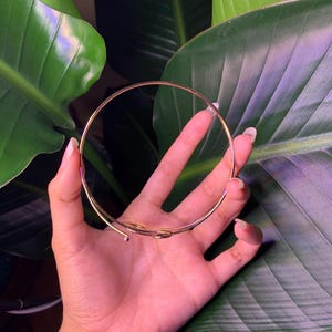 Peut inclure: Un bracelet jonc en m&eacute;tal dor&eacute; au design simple et minimaliste. Le bracelet est ouvert et l&eacute;g&egrave;rement incurv&eacute;.