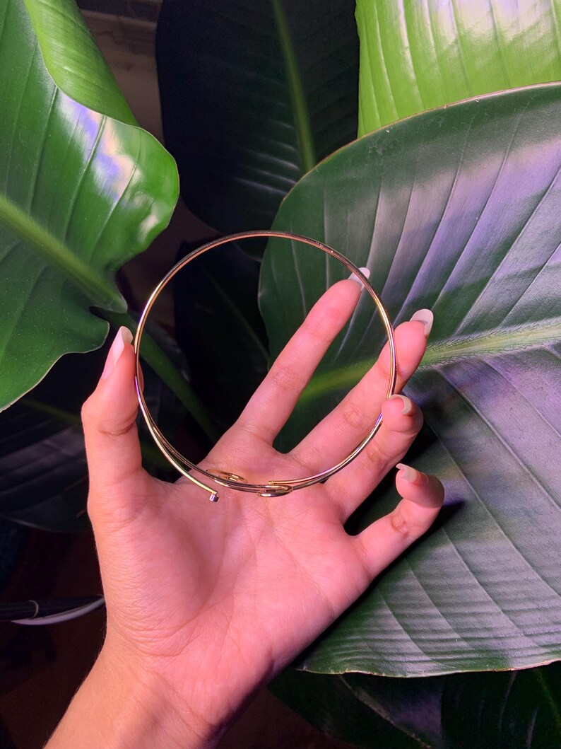 Peut inclure: Un bracelet jonc en m&eacute;tal dor&eacute; au design simple et minimaliste. Le bracelet est ouvert et l&eacute;g&egrave;rement incurv&eacute;.