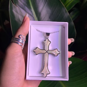 May include: A silver chain necklace with a white mother of pearl cross pendant. The cross has a silver outline and is in a box.