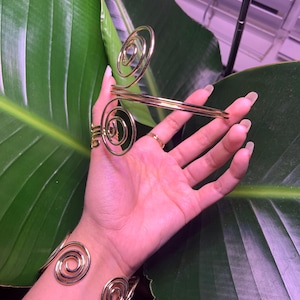 May include: A set of two gold-toned spiral bracelets. The bracelets are made of thin metal and have a delicate, feminine look.