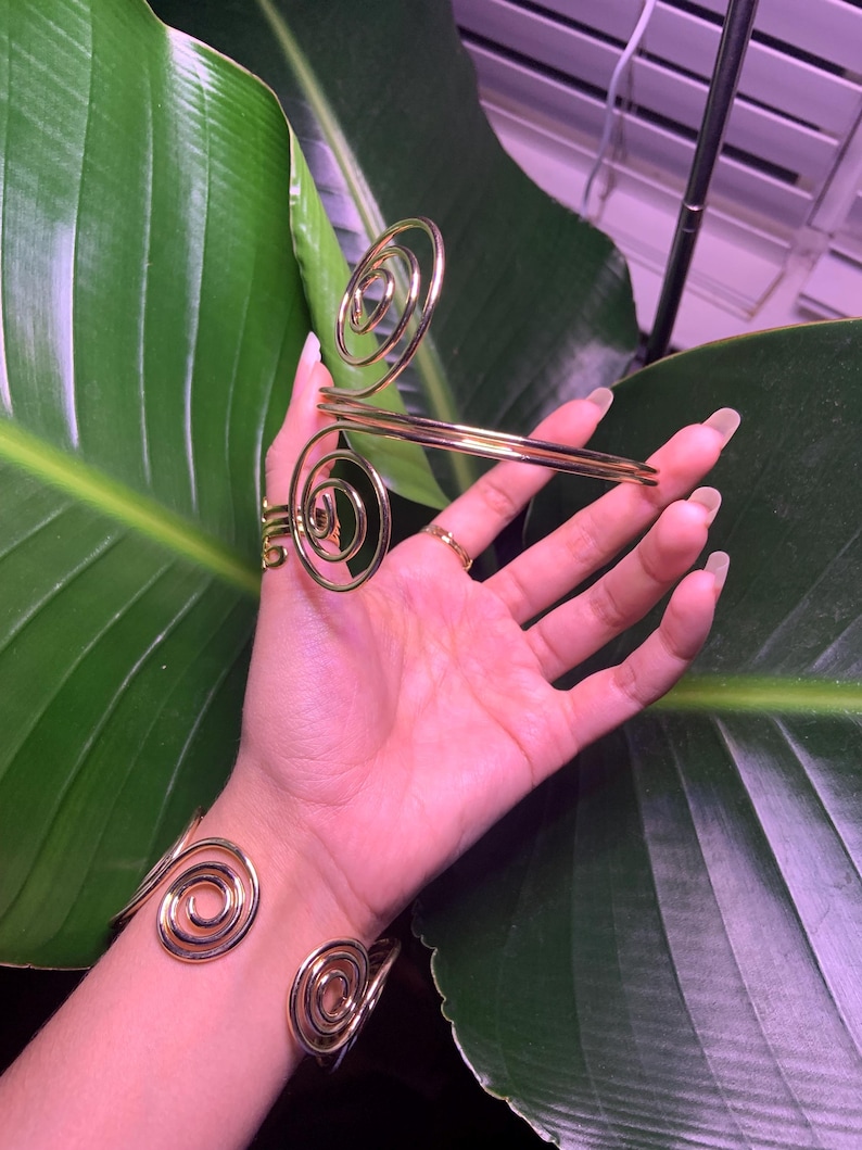 May include: A set of two gold-toned spiral bracelets. The bracelets are made of thin metal and have a delicate, feminine look.