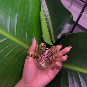 May include: A gold-toned spiral cuff bracelet with a circular design. The bracelet is made of wire and has a delicate, intricate look.