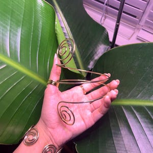 May include: A set of two gold-toned spiral wire bracelets. The bracelets are made of thin wire that is twisted into a spiral shape. The bracelets are worn on the wrist and are adjustable in size.