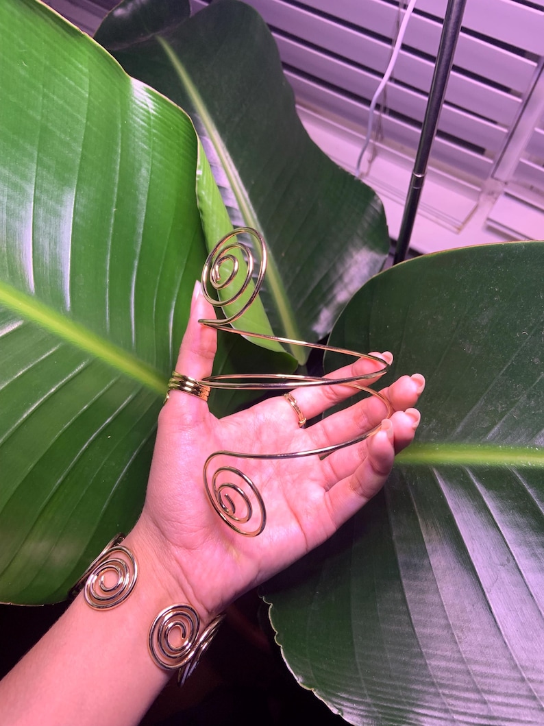 May include: A set of two gold-toned spiral wire bracelets. The bracelets are made of thin wire that is twisted into a spiral shape. The bracelets are worn on the wrist and are adjustable in size.