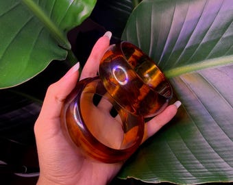 May include: Two amber-colored plastic bangles stacked on top of each other. The bangles are smooth and shiny.