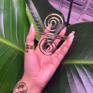 May include: A set of three gold-toned spiral bracelets. The bracelets are made of wire and are designed to fit around the wrist and fingers.