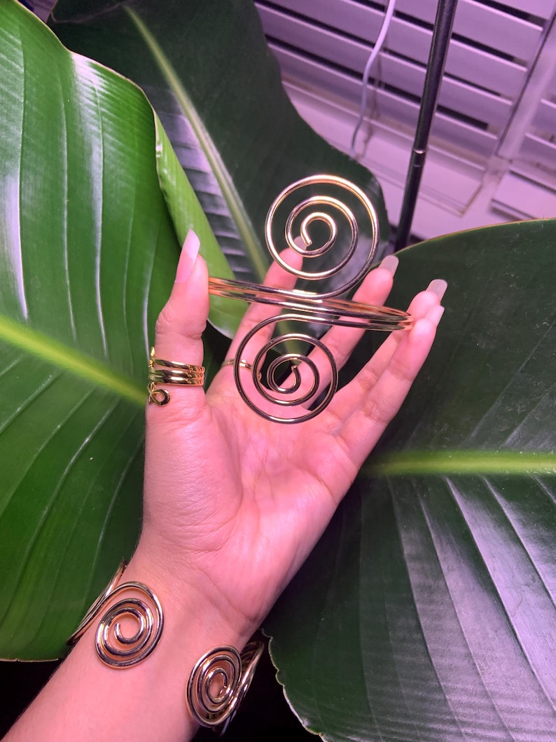 May include: A set of three gold-toned spiral bracelets. The bracelets are made of wire and are designed to fit around the wrist and fingers.