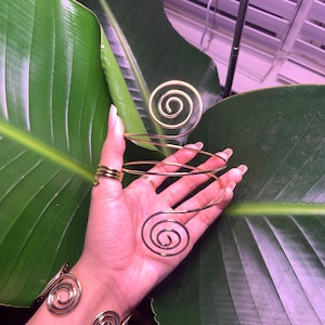 May include: Gold wire bracelet with a spiral design. The bracelet is worn on a person's wrist and arm.