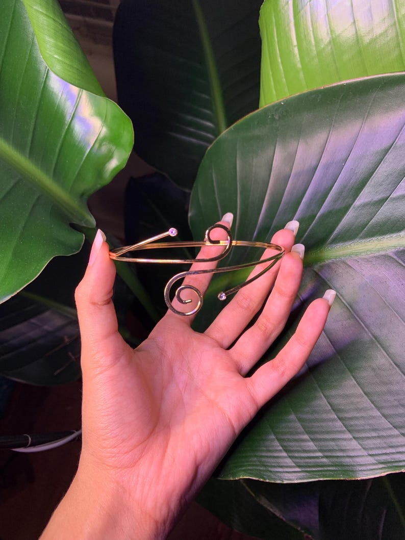 Peut inclure: Un bracelet dor&eacute; avec un design d&eacute;licat en spirale et deux petits strass transparents.