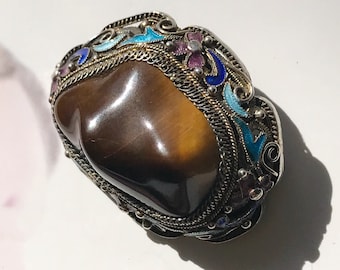 Könnte beinhalten: Ein brauner Tigerauge-Stein, der in einen silbernen Ring mit einem detaillierten Emaille-Design in Blau, Rosa und Weiß gefasst ist.