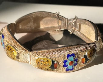 Könnte beinhalten: Ein silbernes Armband mit einem zarten Maschenmuster und bunten Emaille-Akzenten. Das Armband zeigt ein sich wiederholendes Muster aus Marienkäfern und Blumen in Blautönen, Gelb, Rot und Orange.