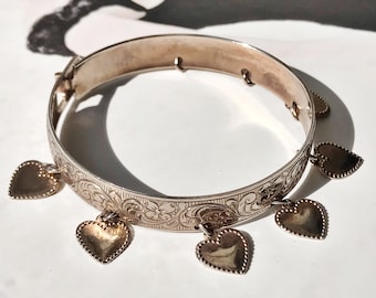 Könnte beinhalten: Ein silbernes Armreif-Armband mit einem gravierten Blumenmuster und fünf baumelnden Herzanhängern.