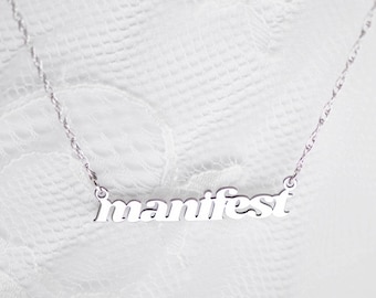 Könnte beinhalten: Silberne Halskette mit dem Wort "manifest" in einer fetten, kursiven Schrift.