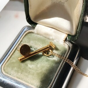 May include: A gold necklace with a small, round pendant in the shape of a golf club. The necklace is in a green velvet jewelry box.