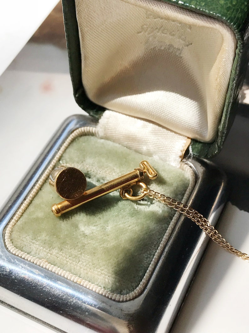 May include: A gold necklace with a small, round pendant in the shape of a golf club. The necklace is in a green velvet jewelry box.