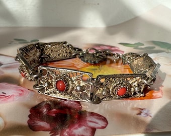 Könnte beinhalten: Ein silbernes Filigranarmband mit roten Korallenperlen. Das Armband ist aus filigraner, kunstvoller Metallarbeit gefertigt und hat ein florales Design.