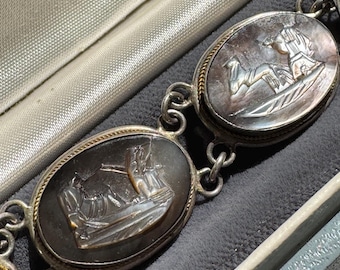 Könnte beinhalten: Ein silbernes Armband mit ovalen schwarzen und weißen Kameen-Anhängern. Jeder Anhänger zeigt eine detaillierte gravierte Szene eines Schiffes mit Figuren.