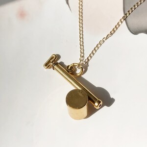 May include: A gold chain necklace with a pendant that looks like a small, cylindrical key. The key has a small, round head and a long, thin shaft.