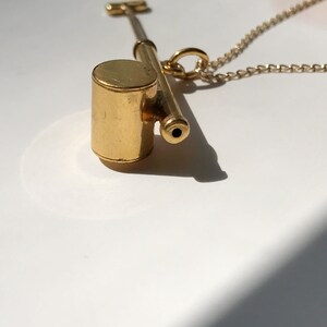 May include: A gold whistle necklace with a round, cylindrical whistle attached to a gold chain.