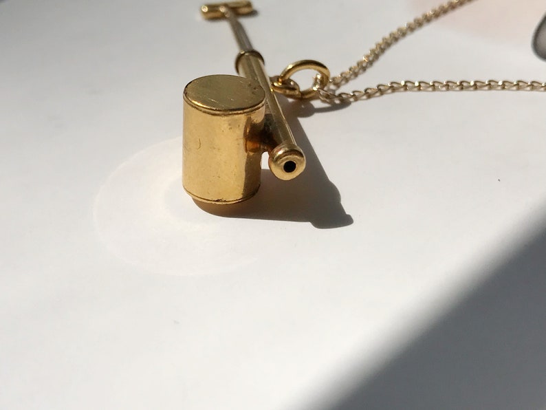 May include: A gold whistle necklace with a round, cylindrical whistle attached to a gold chain.
