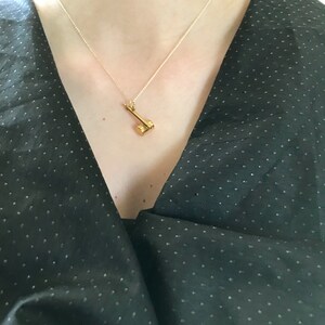 May include: A gold necklace with a small hammer pendant. The necklace is worn by a person wearing a black, polka dot shirt.