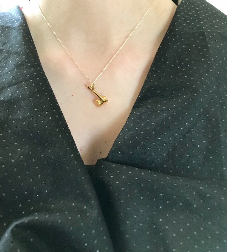 May include: A gold necklace with a small hammer pendant. The necklace is worn by a person wearing a black, polka dot shirt.
