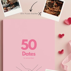 Könnte beinhalten: Ein rosa Notizbuch mit dem Text "50 Dates to remember" und einer Strichzeichnung von zwei sich haltenden Händen. Das Notizbuch ist von rosa Herzen und einem rosa Band umgeben.