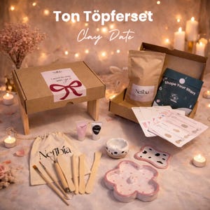 Könnte beinhalten: Ein Töpferset mit dem Text "Ton Töpferset Clay Date". Das Set enthält eine Box mit Schleife, einen Beutel mit dem Text "Nefibía", Werkzeuge, Ton und eine blütenförmige Schale. Ebenfalls enthalten ist eine kleine Schale mit schwarzen Punkten.
