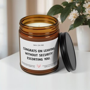 以下が含まれることがあります： 白いラベルに「WAX ON FIRE CONGRATS ON LEAVING WITHOUT SECURITY ESCORTING YOU.」と書かれた茶色のガラス製のキャンドルジャー。このキャンドルは、大豆ベースで無毒です。