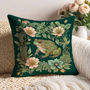 May include: A green throw pillow with a floral design featuring a green frog, pink flowers, and green leaves on a dark green background.