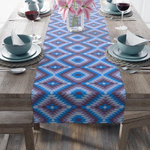 May include: A blue and purple geometric patterned table runner with a diamond pattern. The runner is on a wooden table with place settings on either side.