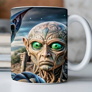 May include: White ceramic mug with a colorful image of an alien with green eyes and intricate facial markings. The alien is looking directly at the viewer.