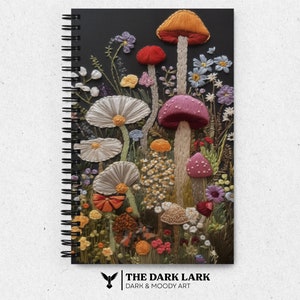 Può includere: Un quaderno a spirale nero con un designo ricamato colorato di funghi e fiori. Il testo "THE DARK LARK DARK & MOODY ART" è in fondo al quaderno.