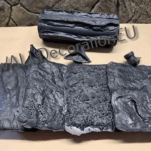 Puede incluir: Un conjunto de piezas de decoración de pared de espuma texturizada negra, que incluye una forma de tronco y varias piezas planas. Las piezas están diseñadas para parecerse a roca o piedra.