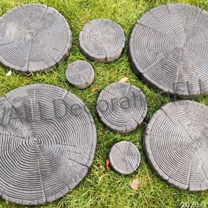 May include: A set of seven gray concrete stepping stones shaped like tree rings. The stones are arranged in a circle on a bed of green grass.