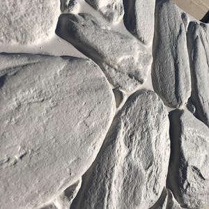Puede incluir: Primer plano de una pared de piedra gris hecha de piedras de formas irregulares. Las piedras tienen una superficie rugosa y texturizada y están dispuestas en un patrón aleatorio.