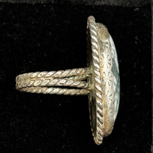 May include: A silver ring with a green and white stone set in a rope-like band.