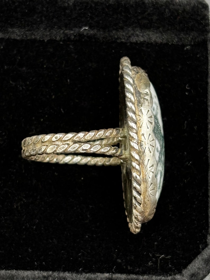 May include: A silver ring with a green and white stone set in a rope-like band.